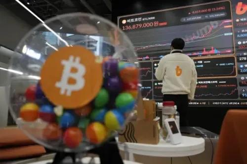 ارتفاع سعر البيتكوين إلى 136,879,000 وون، مع شخص يتفاعل مع شاشة تعرض بيانات السوق في مركز تداول للعملات الرقمية.
