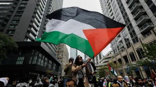 امرأة تحمل علم فلسطين في مظاهرة حضرها حشد كبير، تعبر عن دعمها لقضية فلسطين وسط مباني المدينة.