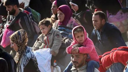 عائلات فلسطينية نازحة تسير معًا، تحمل حقائب صغيرة، معبرة عن الصمود وسط أزمة إنسانية حادة في غزة.