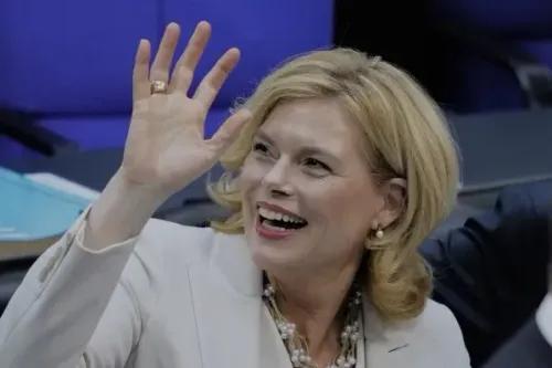 جوليا كلوكنر، رئيسة البرلمان الألماني الجديدة، تبتسم وتلوح بيدها أثناء جلسة انتخابها، مع خلفية زرقاء تعكس أجواء البرلمان.