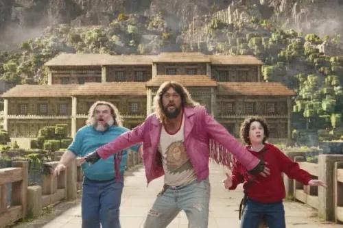 ثلاث شخصيات رئيسية في فيلم "A Minecraft Movie" تتفاعل في مشهد مثير، مع خلفية مناظر طبيعية خيالية ومباني مستوحاة من اللعبة.