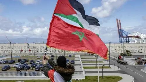 رجل يحمل علم المغرب مع العلم الفلسطيني في خلفية ميناء، يعبر عن الغضب من التعاون العسكري مع إسرائيل.