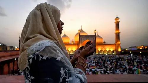 امرأة ترتدي الحجاب تصلي في المساء أمام مسجد كبير، مع خلفية تضم حشودًا من المصلين، مما يعكس الأجواء الروحية في سياق قانون الوقف الجديد في الهند.