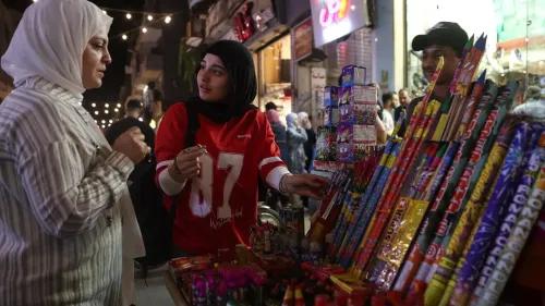امرأتان تتحدثان في سوق شعبي، بينما تبيع فتاة صغيرة ألعاب نارية ملونة، مما يعكس أجواء الاحتفالات في المجتمعات المسلمة.