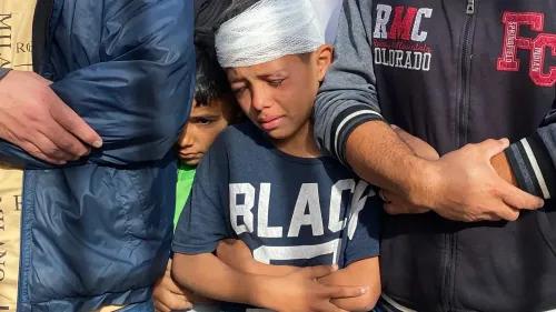 طفل مصاب برباط على رأسه، يظهر الحزن والخوف، يقف بجوار طفل آخر ورجال، في سياق الأزمات الإنسانية في غزة.