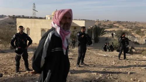 مواطن فلسطيني يقف أمام منزله المهدوم في أم الحيران، بينما تراقبه قوات الشرطة الإسرائيلية في الخلفية.