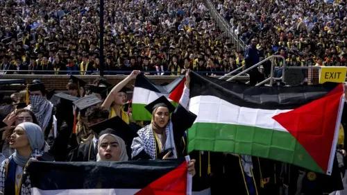 طلاب متخرجون في جامعة ميشيغان يرفعون الأعلام الفلسطينية خلال حفل التخرج، وسط حشد كبير من الحضور، تعبيرًا عن دعمهم للقضية الفلسطينية.