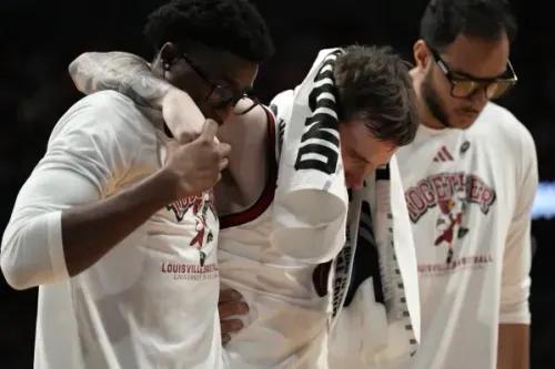 لاعب لويزفيل راين سميث يتلقى الدعم من زملائه بعد إصابته في الكاحل خلال مباراة NCAA، بينما يظهر القلق على وجوههم.