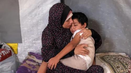 امرأة تحتضن طفلًا في خيمة، تعكس معاناة العائلات الفلسطينية النازحة في غزة بسبب الحرب والتهجير.