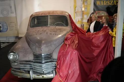 سيارة وارسو M-20 من طراز 1951 تُعرض بعد استعادتها، مع نساء يكشفن عنها في متحف، تعبيراً عن تاريخها في الحقبة السوفيتية.