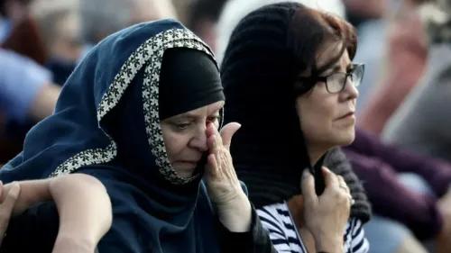 امرأتان، إحداهما ترتدي الحجاب، تعبران عن الحزن خلال مناسبة تذكارية، تعكس مشاعر التأثر بعد أحداث الاعتداءات العنصرية.