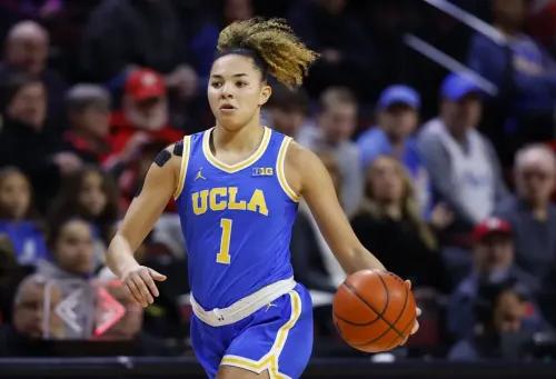لاعبة كرة سلة من جامعة كاليفورنيا في لوس أنجلوس (UCLA) أثناء المباراة، تحمل الكرة وتتحرك نحو الميدان، مع تفاعل الجمهور في الخلفية.