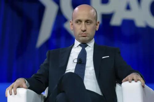 ستيفن ميلر، مستشار سابق للرئيس ترامب، يجلس على منصة مؤتمر مع تعبير جاد، مظهرًا تأثيره على السياسات المتعلقة بالهجرة.