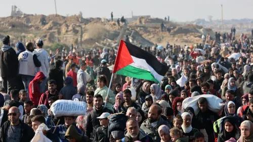 جموع من الفلسطينيين في منطقة غزة يحملون الأعلام ويعبرون عن معاناتهم، وسط أكوام من الحطام، في سياق أزمة النزوح.