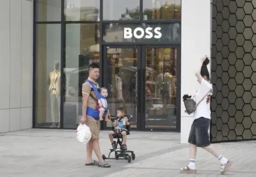 رجل يحمل طفلاً في حمالة أمام متجر، بينما يجلس طفل آخر في عربة. تعكس الصورة التغيرات في سياسات إنجاب الأطفال في فيتنام.