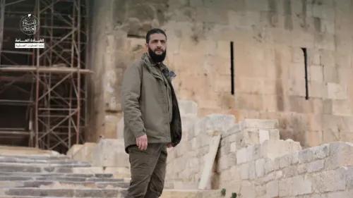 أبو محمد الجولاني يقف على درجات قلعة حلب، محاطًا بأنصاره، ملوحًا بأعلام الثورة السورية بعد استيلاء هيئة تحرير الشام على المدينة.