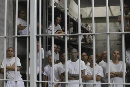 مجموعة من السجناء يرتدون ملابس بيضاء، يقفون داخل زنزانة مكتظة في سجن السلفادور، مع أجواء من التوتر والاحتجاز.