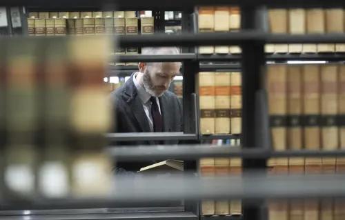 رجل يرتدي بدلة يقف بين رفوف الكتب في مكتبة، يقرأ كتابًا حول تاريخ العبودية وقضية بريغ ضد بنسلفانيا.