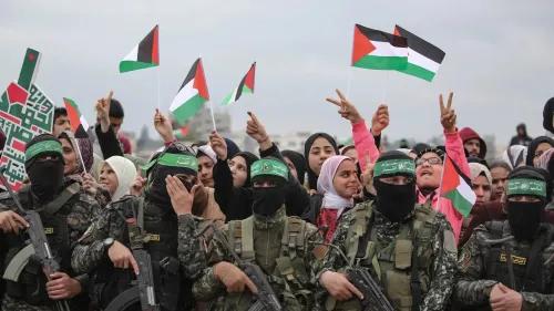 محتجون فلسطينيون يحملون الأعلام الفلسطينية ويظهرون التضامن مع حماس، بينما يقف جنود مسلحون في الخلفية.