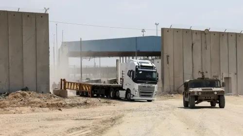 مركبة شحن كبيرة تمر عبر معبر بيت حانون، بينما تتواجد سيارة عسكرية بالقرب من الجدار الفاصل، في سياق جهود تأمين المساعدات إلى شمال غزة.